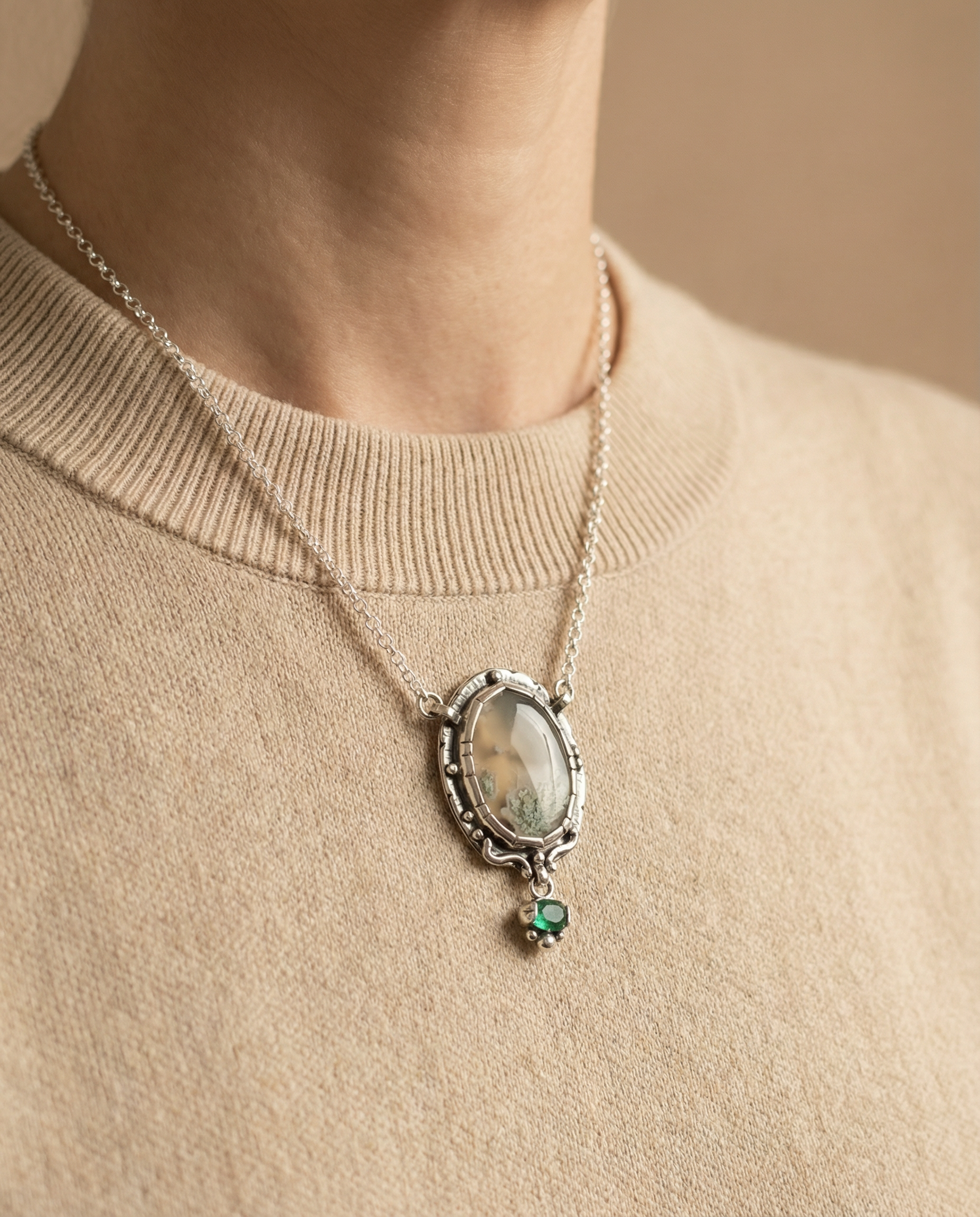 Necklace with a pendant featuring a green gemstone on a beige sweater.
